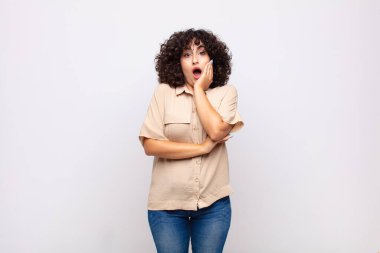 Şok ve inançsızlık içinde ağzı açık, elleri yanağı ve kolu çaprazlanmış, sersemlemiş ve şaşkın bir kadın.