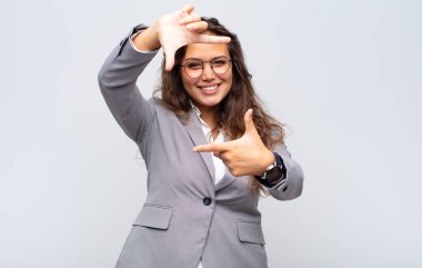 Kadın mutlu, arkadaş canlısı ve pozitif hissediyor, gülümsüyor ve elleriyle bir portre veya fotoğraf çerçevesi yapıyor.