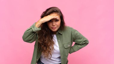 Kadın şaşkın ve şaşkın bakıyor, elleri başının üstünde uzaklara bakıyor, izliyor ya da arıyor.