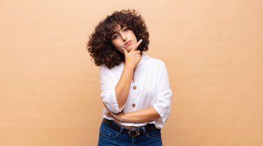 Ciddi, düşünceli ve güvensiz görünen bir kadın. Bir kolu çapraz ve eli çenesinde, seçenekleri değerlendiriyor.