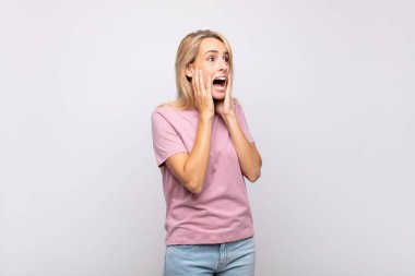 Mutlu, heyecanlı ve şaşırmış hisseden bir kadın, iki eli yüzü havada bir tarafa bakıyor.