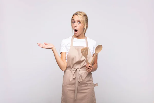 年轻的女厨师看上去很惊讶 很震惊 下颚掉了下来 手里拿着一只张开的手放在旁边的东西 — 图库照片
