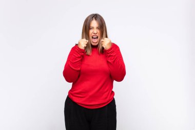 Genç sarışın kadın sinirli, sinirli, sinirli bakışlar ve sıkı yumruklar ile agresif bir şekilde bağırıyor.