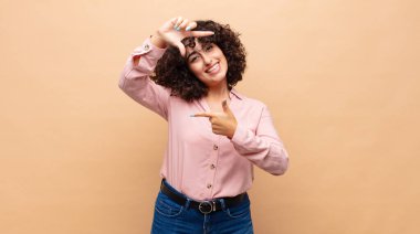 Kadın mutlu, arkadaş canlısı ve pozitif hissediyor, gülümsüyor ve elleriyle bir portre veya fotoğraf çerçevesi yapıyor.