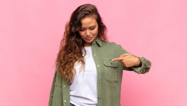 Neşeli bir şekilde gülümseyen, aşağıya bakan ve göğsünü gösteren bir kadın.