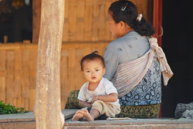 Luang Prabang, Laos - 13 Şubat 2007: Anne ve çocuk onların evinde Luang Prabang, Laos yakınındaki geleneksel köy dışında oturmak.