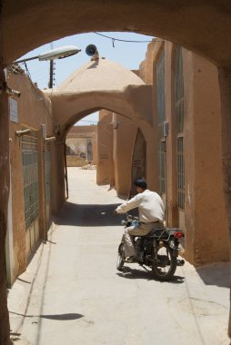 Yazd, Iran - Haziran 17, 2007: Kimliği belirsiz Yezd, İran'ın tarihi bölümünde kil kaplı duvarlı dar sokak tarafından Motosiklet sürmek.