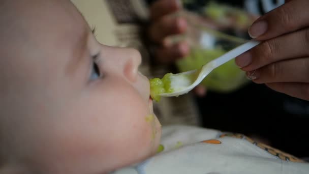 Klein kind eet van de plastic lepel groene puree in slow motion. — Stockvideo