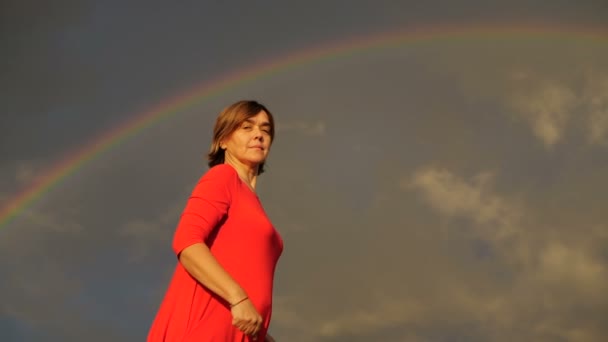 Arco iris al fondo. Mujer en vestido rojo muestra pulgares y sonrisa . — Vídeo de stock