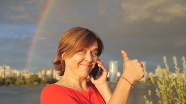 Happy middle aged woman shows thumb and talks with phone in slow motion. — Stock Video