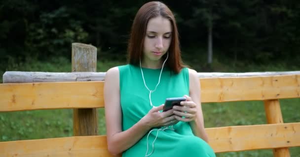 Junge Frau ruht sich auf Bank aus und hört Musik mit Kopfhörern. — Stockvideo