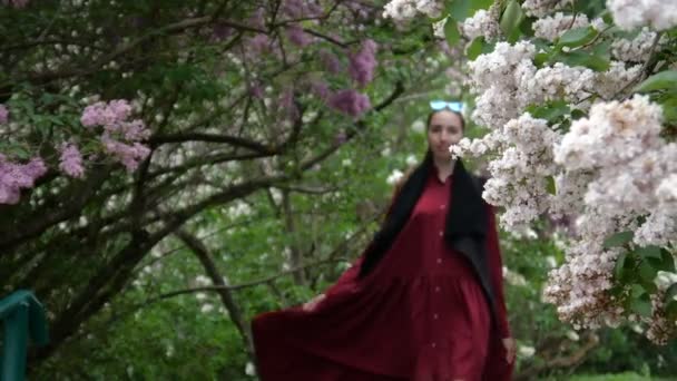 Una joven morena camina en el jardín con una flor lila — Vídeo de stock