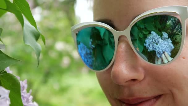 Сирень крупным планом отражается в солнцезащитных очках на лице молодой девушки — стоковое видео