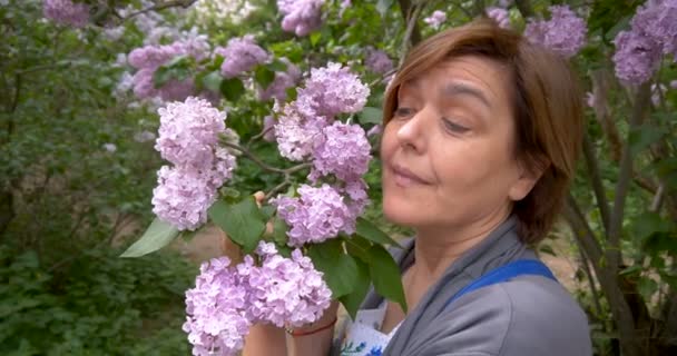 Eine Frau mittleren Alters lächelt im Park neben fliederfarbenen Blumen. Nein.