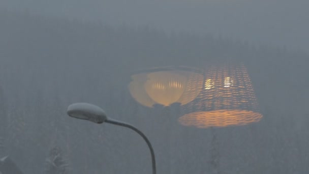 Snöfall i bergen - speglar lampan i fönstret. — Stockvideo
