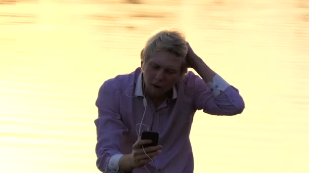 Homem romântico senta-se em uma margem do lago com caminho dourado do sol — Vídeo de Stock