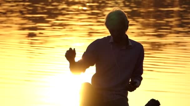 Hombre rubio se sienta y baila en una orilla del lago en slo-mo — Vídeos de Stock