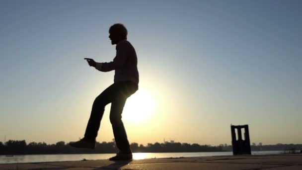 Веселий чоловік танцює джон на березі річки влітку в шлю-мо — стокове відео
