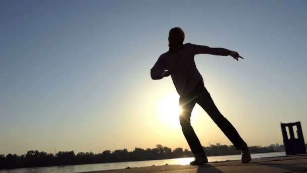 スローモーションで夏の素敵な夕日を川の土手に積極的に踊り若い細身の男の陽気な眺め 彼はエネルギーのボールのように見える — ストック動画