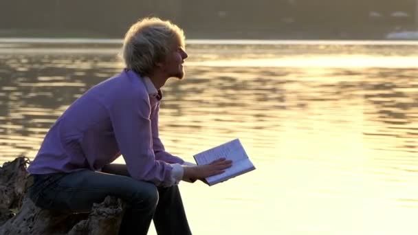 Happy journalist reads a boot to write an article at a lake — Stock Video