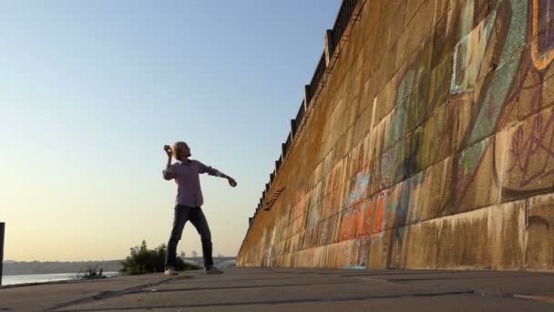 若い男は、スローモーションで川の土手の石壁の上のボールを投げる — ストック動画