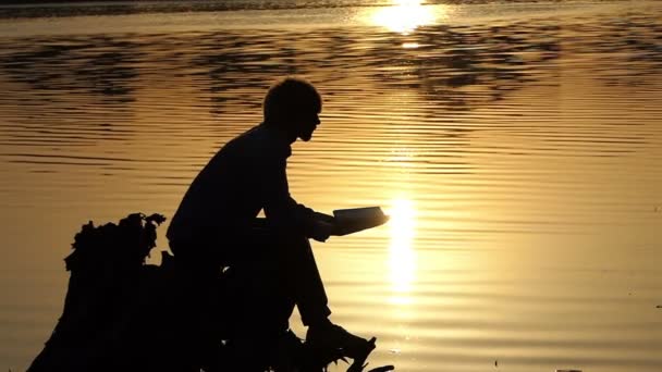 Young man reads a play on a splendid lake bank in slo-mo — Stock Video