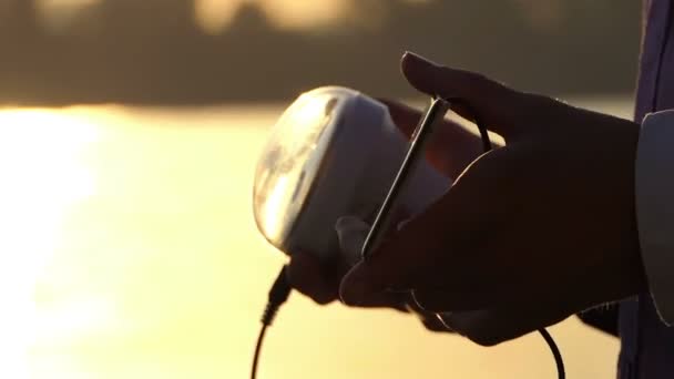 Taschenlampe und Sonnenbatterie sind bei Sonnenuntergang in männlicher Hand — Stockvideo