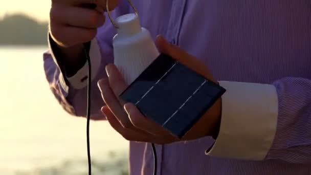 Современный фонарик и солнечная батарея в руках на закате — стоковое видео