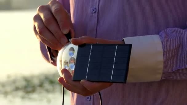 Скляний ліхтарик і сонячна батарея знаходяться в руках під час заходу сонця — стокове відео