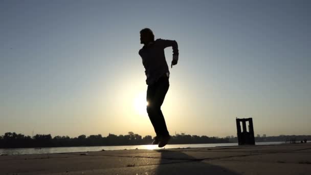 Cheery man dansar disco aktivt på en flodbank i slo-mo — Stockvideo