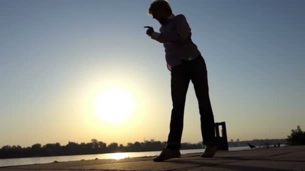 Joven bailarina muestra pases modernos en una orilla del río al atardecer en slo-mo — Vídeo de stock