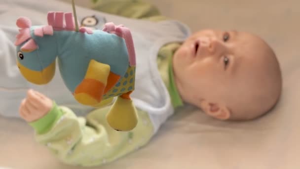 Newborn baby lays on his bed and looking on the toys. — Stock Video