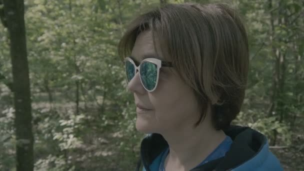 Kobieta w średnim wieku w okulary przeciwsłoneczne w lesie. — Wideo stockowe