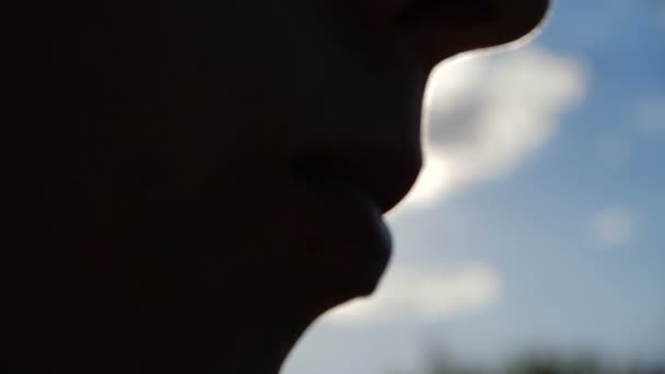 Силует жіночого обличчя їсть якусь їжу з ложки на відкритому повітрі в повільному русі — стокове відео