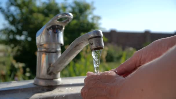 Female hands cleaning each other under a stream of water in a garden in slo-mo — Stock Video