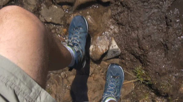 Hairy male legs in snickers going in a mountain rill with stones