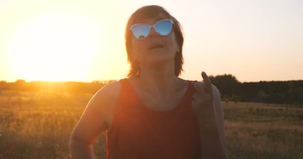 Femme heureuse en lunettes de soleil dansant dans un champ au coucher du soleil en été — Video