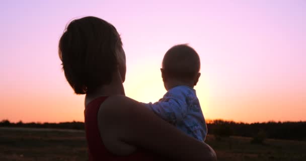 Mujer alegre con un niño en las manos mirando espléndido atardecer al aire libre en slo-mo — Vídeos de Stock