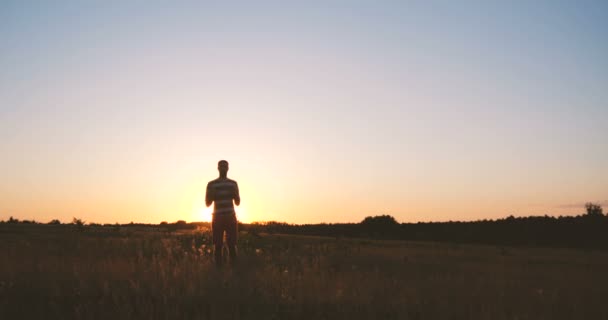 幸せな若い男ジャンプとスローモーションで夕暮れ時のフィールドに足を曲げ — ストック動画