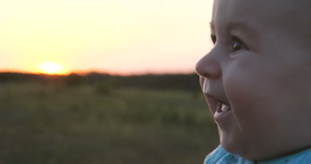Ευτυχισμένο μωρό χαμογελά σε ένα μεγάλο πεδίο κατά το ηλιοβασίλεμα το καλοκαίρι σε αργή κίνηση — Αρχείο Βίντεο