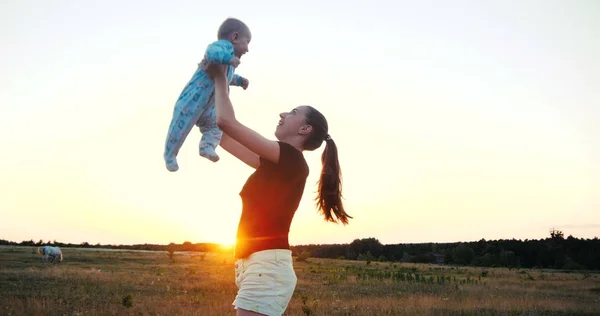 Emotional young woman raising her baby in hands in a field at sunset in slo-mo Stock Image