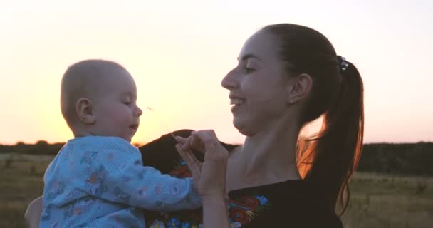 Glad ung mamma leker med hennes kid i ett fält vid solnedgången i slo-mo — Stockvideo