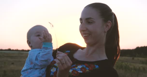 Happy baby och hennes barn palying med varandra i ett fält vid solnedgången i slo-mo — Stockvideo
