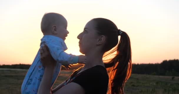 Perfil alegre de una madre joven manteniendo a su bebé en manos al atardecer en slo-mo — Vídeos de Stock