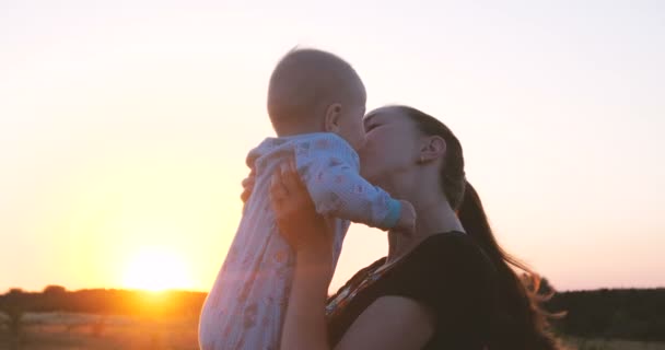 Ευτυχισμένη γυναίκα φιλιά το μωρό της σε ένα πεδίο στο ηλιοβασίλεμα σε αργή κίνηση. — Αρχείο Βίντεο