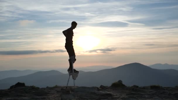 Man på styltor går på toppen av berget vid solnedgången. — Stockvideo