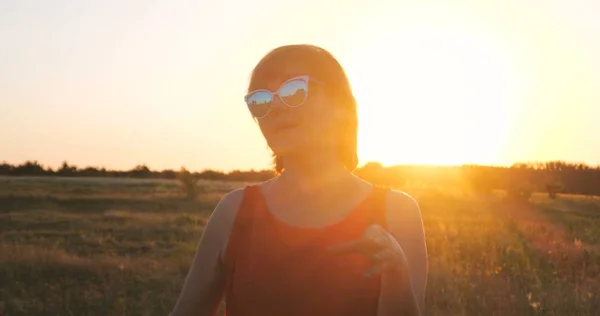 Happy woman in sunglasses dancing in a field at sunset in summer