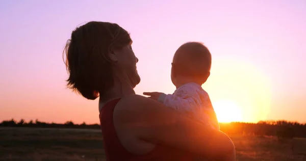 Fröhliche Frau mit einem Kind in der Hand, das den herrlichen Sonnenuntergang im Freien betrachtet — Stockfoto