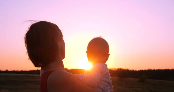 Mujer alegre con un niño en las manos mirando espléndido atardecer al aire libre —  Fotos de Stock