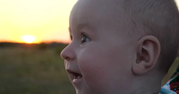 Happy baby looking at his mother and smiling in a field at sunset — Stock Photo, Image